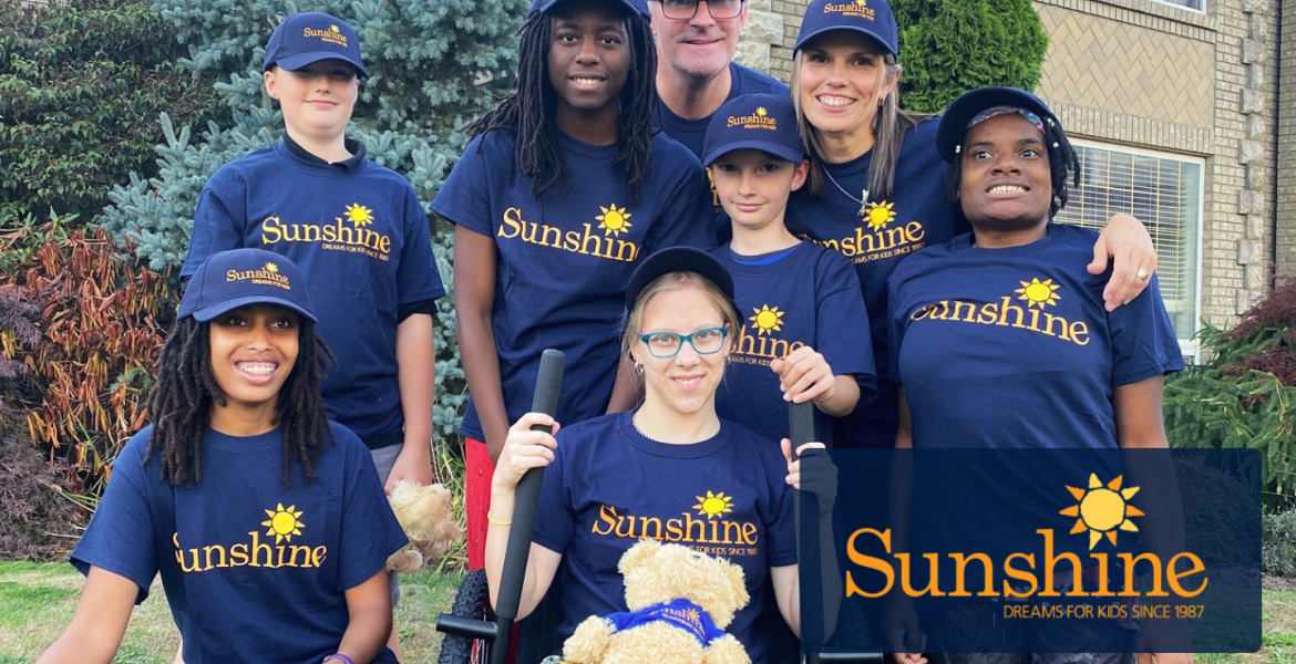Chenoa sits in her new all-terrain wheelchair surrounded by friends and family wearing navy blue Sunshine t-shirts and hats