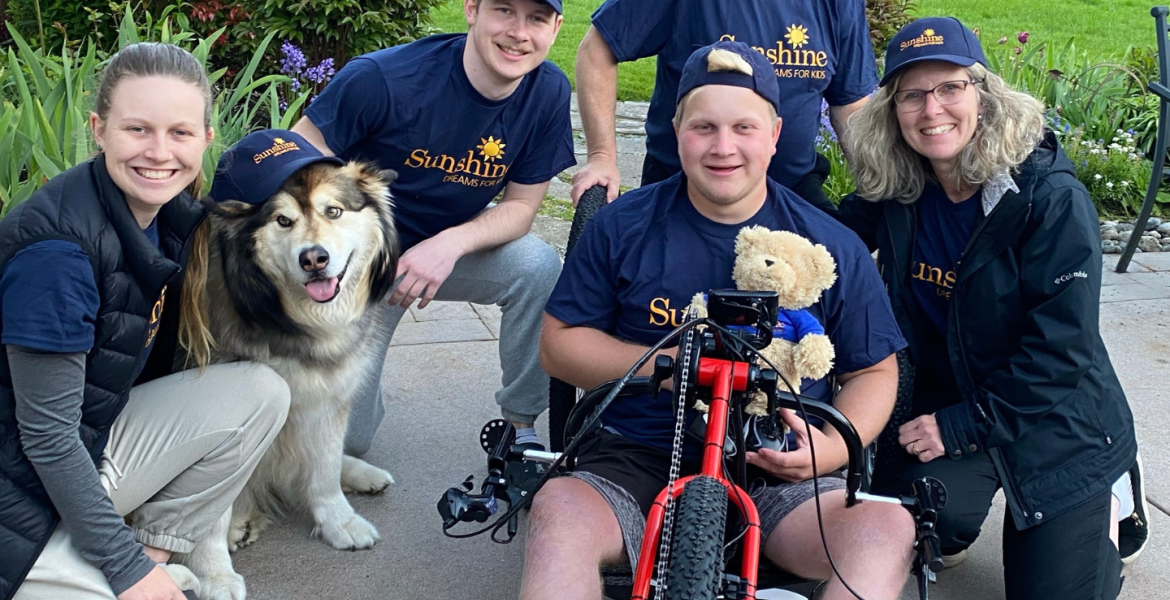 Thomas is seated on his red handcycle surrounded by his family and his husky dog