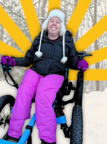 Karissa wears winter jacket and pink snow pants seated in an all-terrain rig in front of snow pile