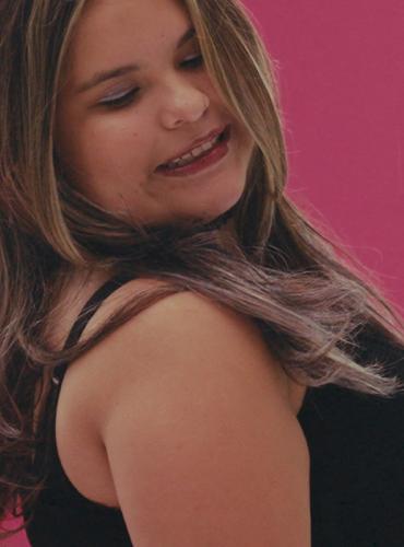 Scarlette, a blind indigenous teen, poses like a model with her eyes closed, looking over shoulder. Pink background