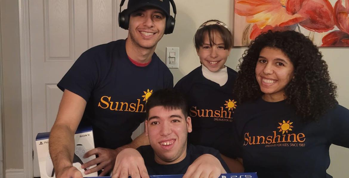 Ali seated with hands on PS5 box with family smiling behind him