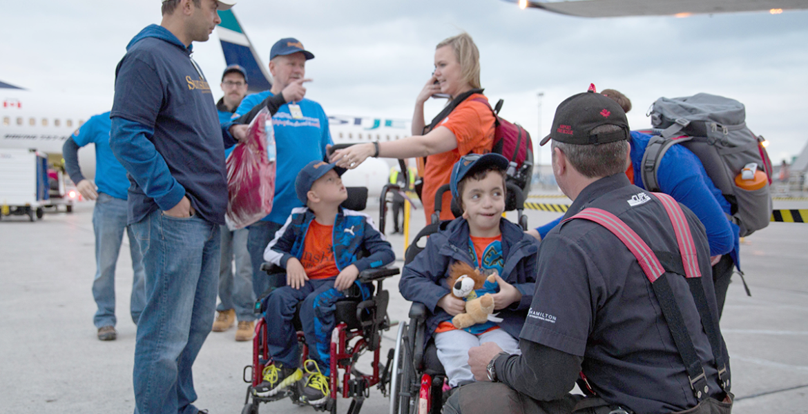 Two boys in wheelchairs on the tarmac with fireman in foreground