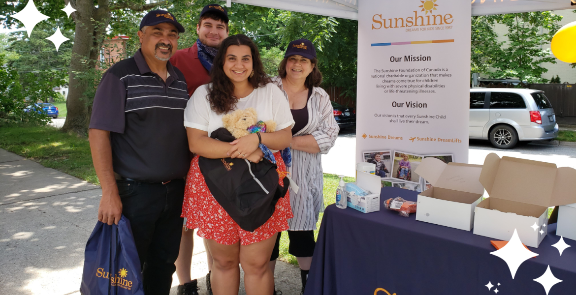 Faith and her family gathered together and smiling under a gazebo in a park standing next to a Sunshine Foundation banner.