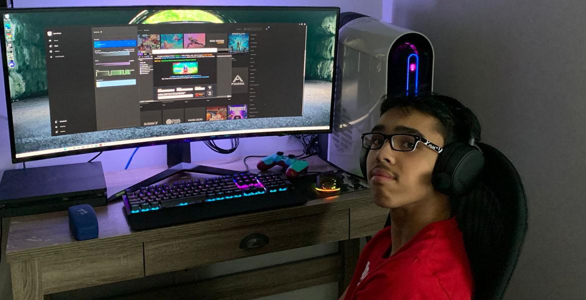 Teenage boy with dark hair, glasses, and headphones sits in front of illuminated gaming keyboard and screen