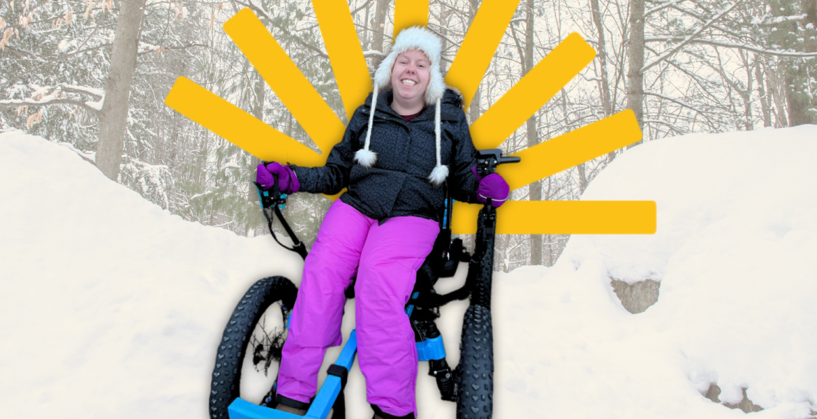 Karissa wears winter jacket and pink snow pants seated in an all-terrain rig in front of snow pile