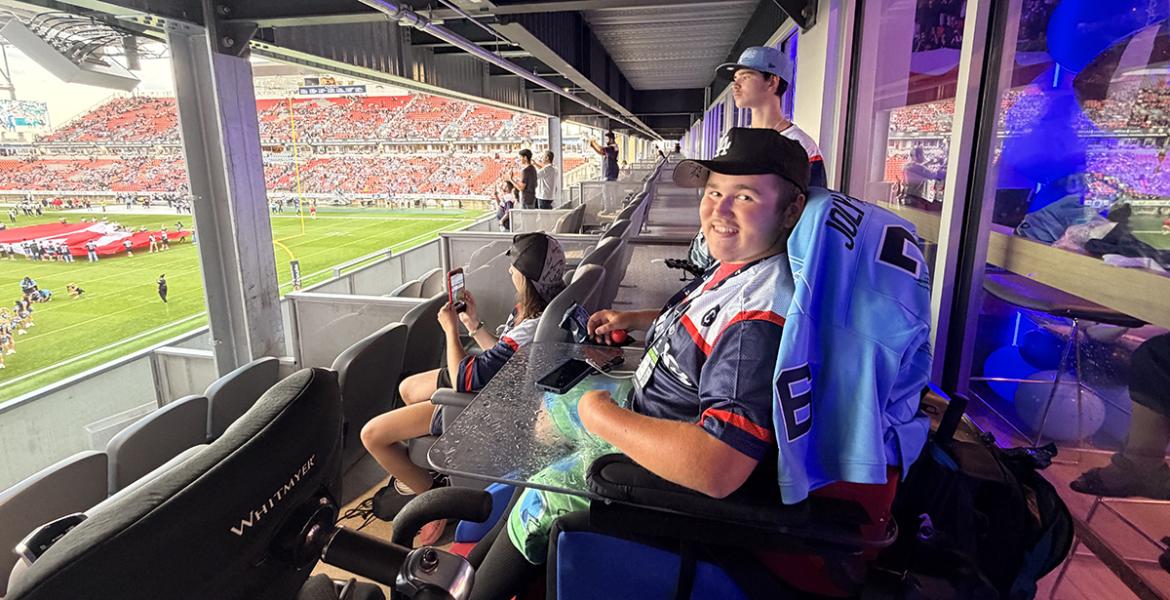 Teen boy in power wheelchair inside a Toronto Argonauts suite watching the football game