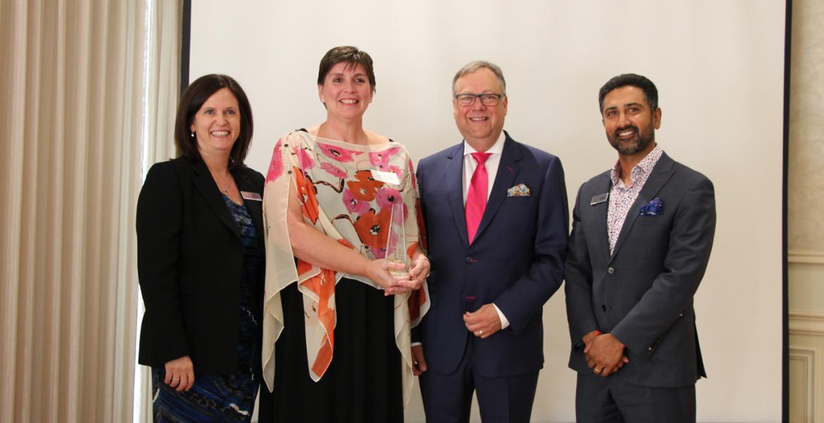 Dr Michelle McNeil holding glass awards statuette surrounded by award presenters