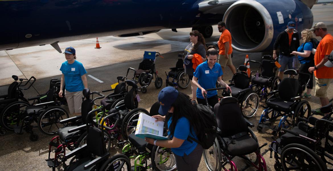 Shine volunteers organize accessibility equipment and wheelchairs on tarmac at airport