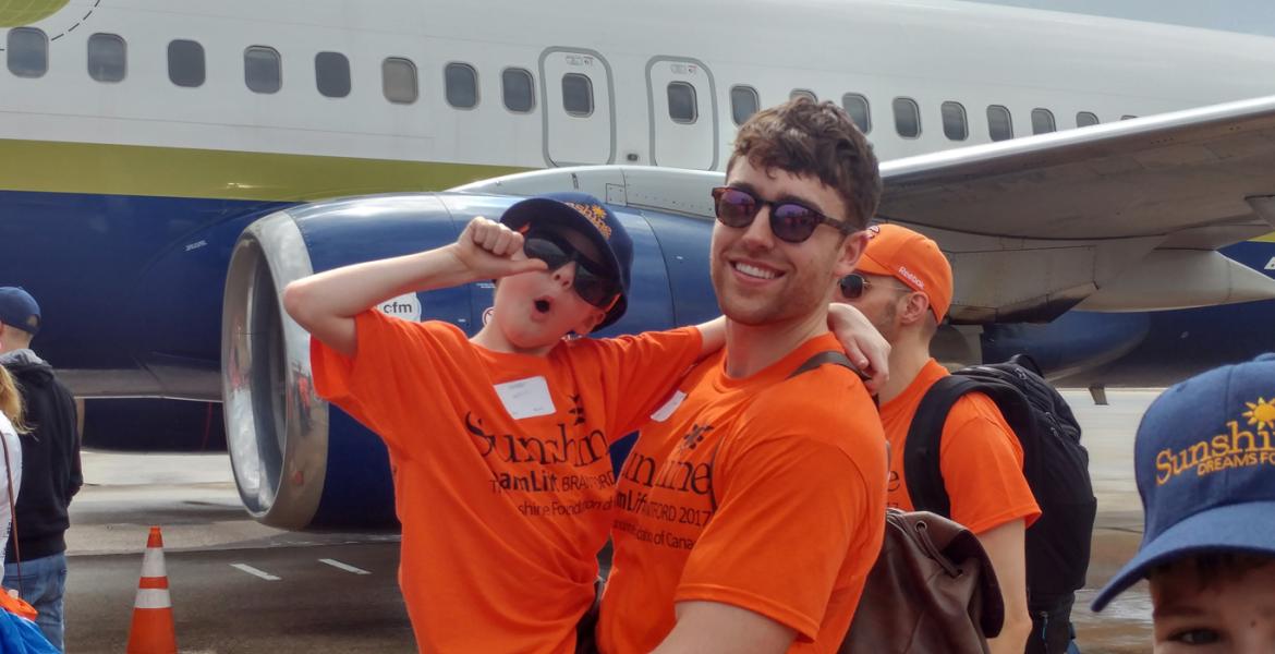 DreamLift participant smiles and gives a thumbs up with plane in background