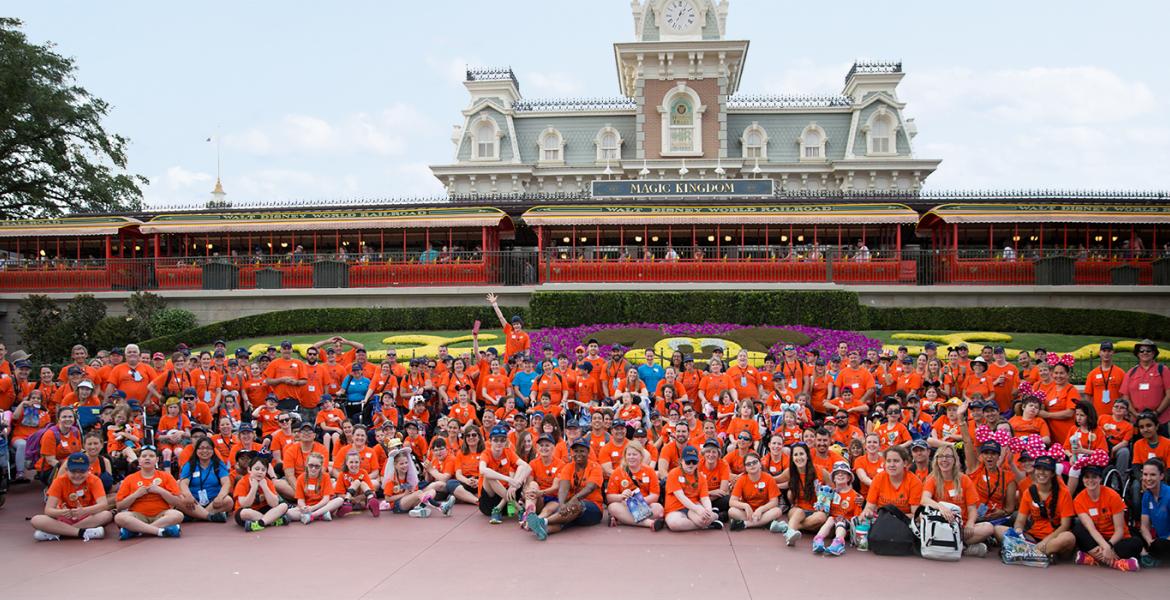 Large group of DreamLift participants and volunteers gather at front entrance to the Magic Kingdom in Disney World.