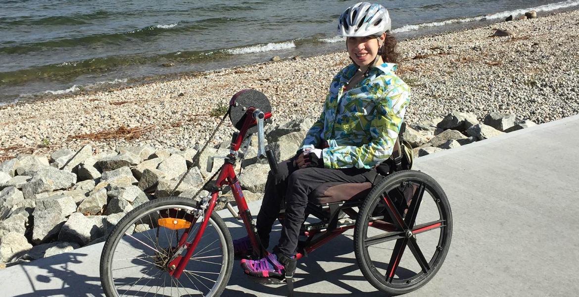 Hannah sits on handcycle bike on path next to a rocky beach