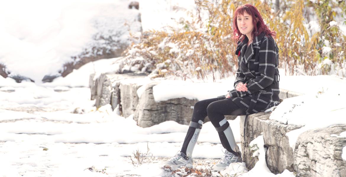 Jaleel wearing black and white coat while seated on rock wall surrounded by snow in a a natural setting