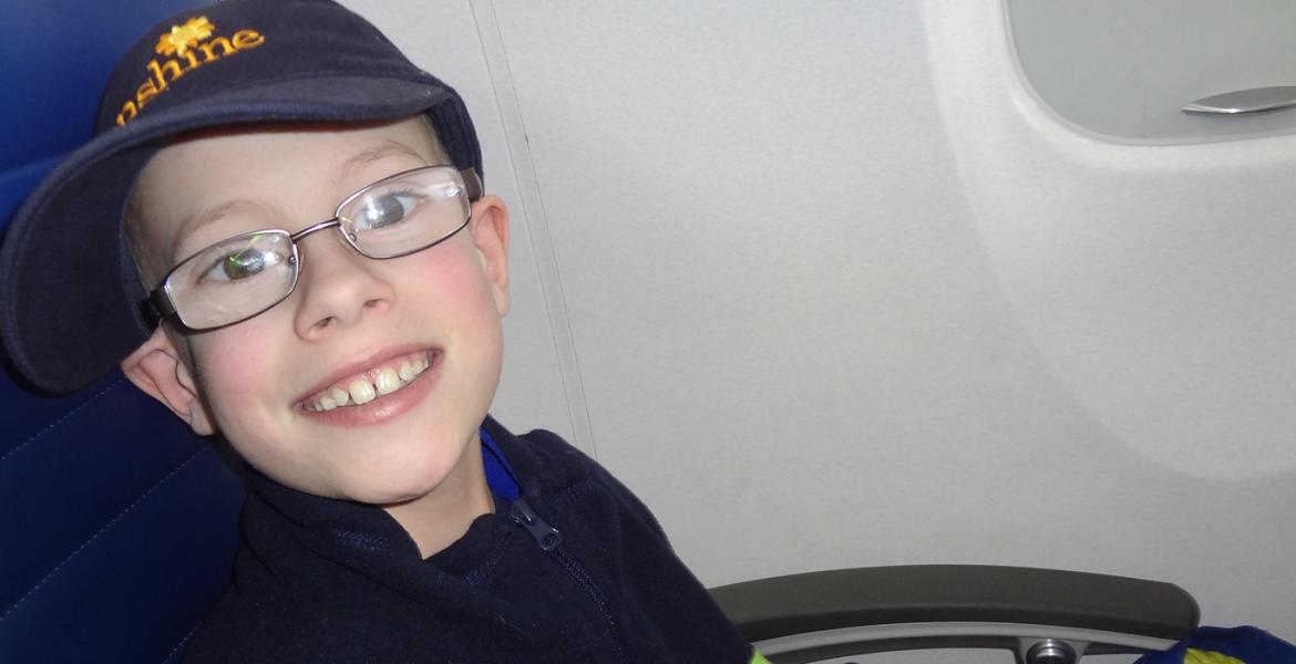 James smiling in a Sunshine Foundation cap seated on in a passenger plane