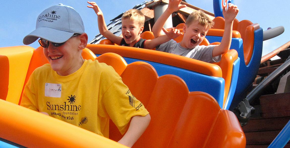 Shine DreamLift participants on a roller coaster in Disney wearing yellow shirts, Jason is a young boy in front riding solo