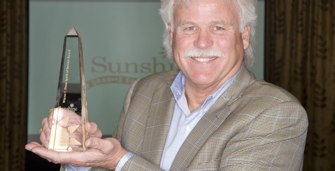 John wearing a sport coat and holding a glass awards statuette.