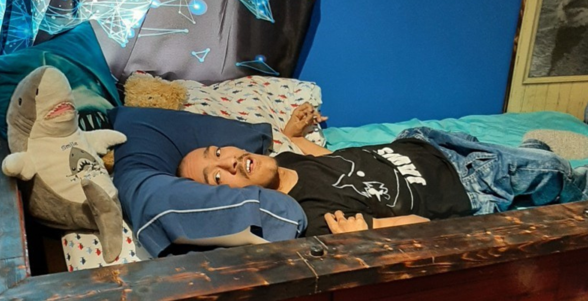 Juwann lying in Jaws themed ship bed next to stuffed shark plushie