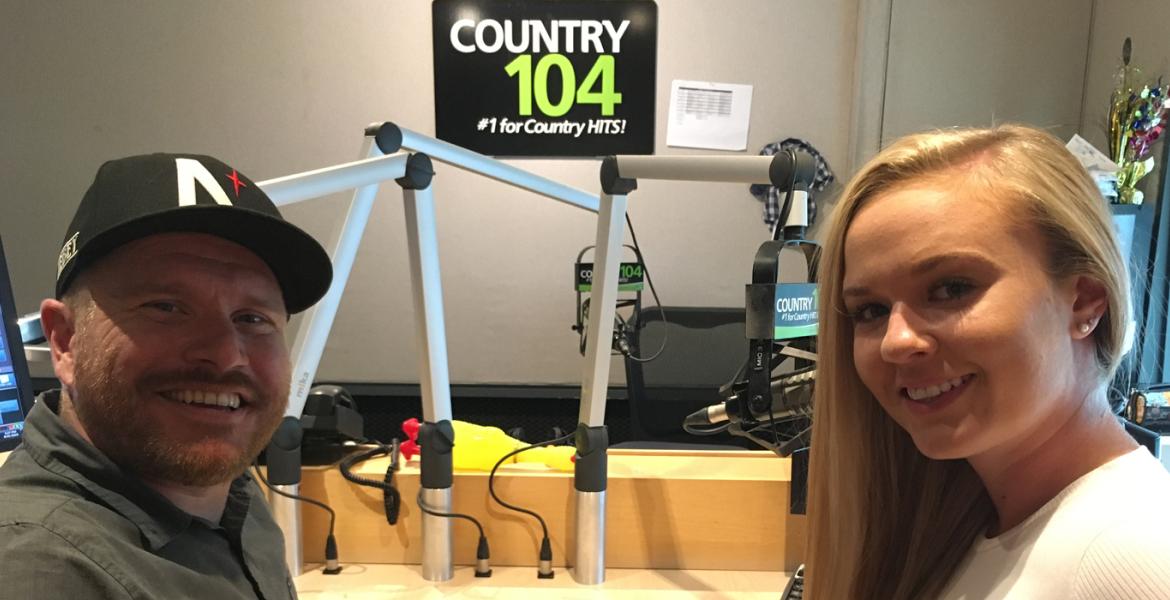 Maddy and her dad next to microphones with Country 104 radio sign on wall behind