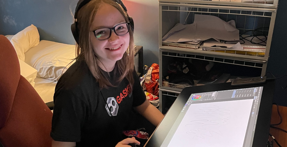 Lily wearing headphones sitting at a desk in front of large digital drawing tablet