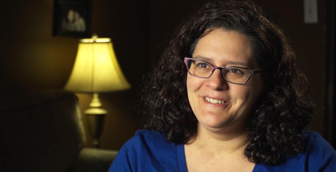 Close up of Sarah smiling in a blue shirt and purple glasses