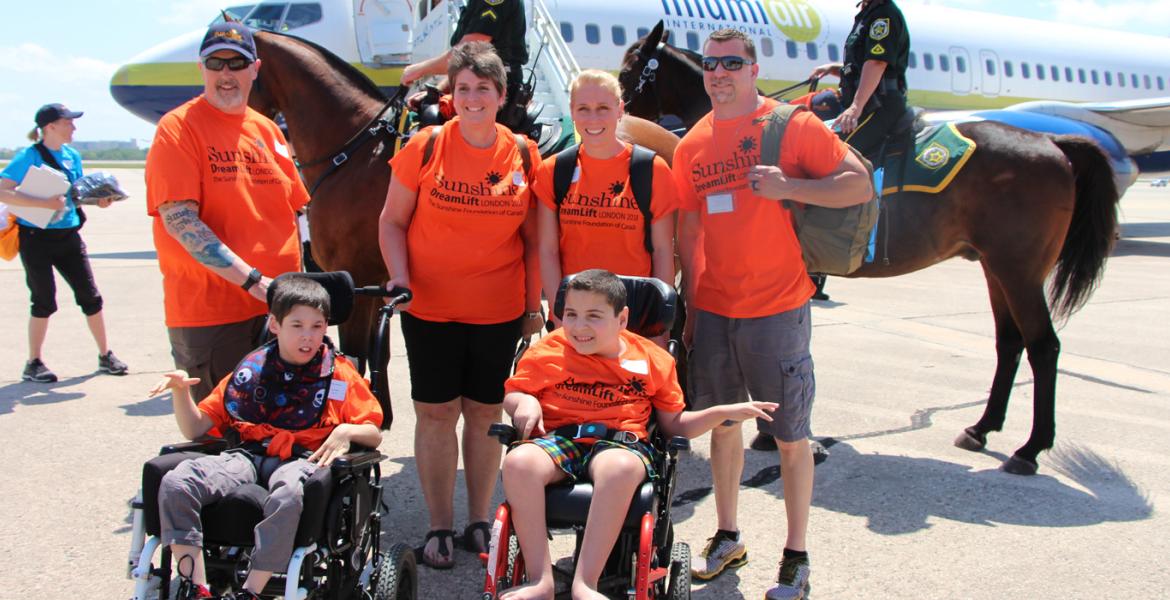 DreamLift recipient Ali smiles with group in front of plane on tarmac