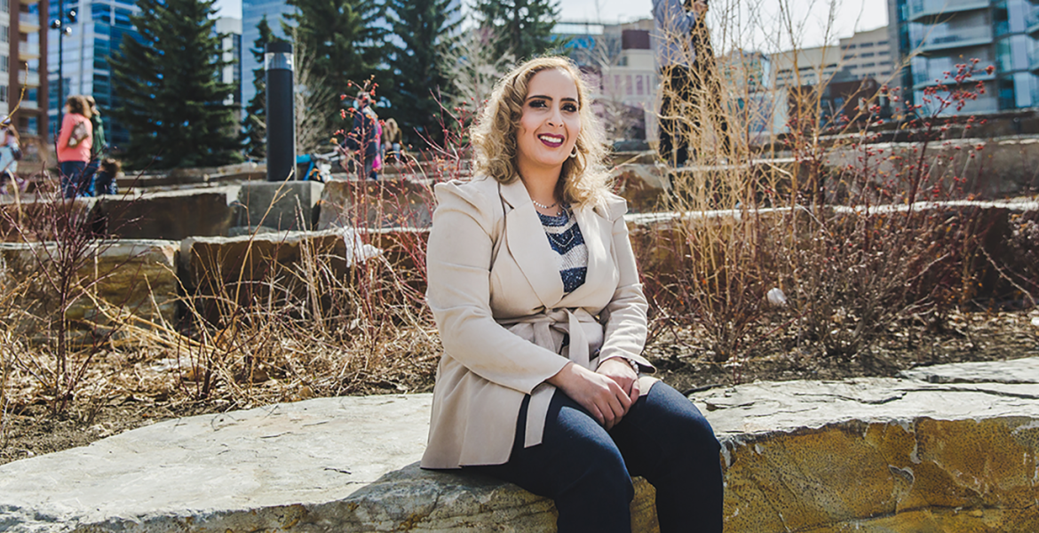 Razan in a beige coat seated on a rock bench in a park